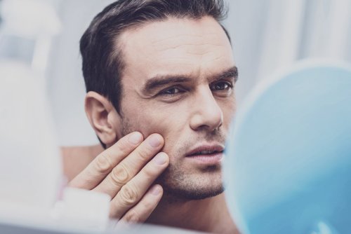 男子在鏡子中檢查臉部，觸摸面頰。